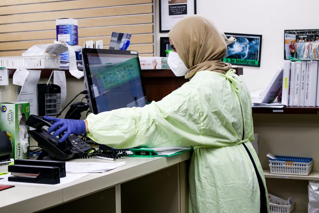 nurse wearing protective gear at a computer workstation