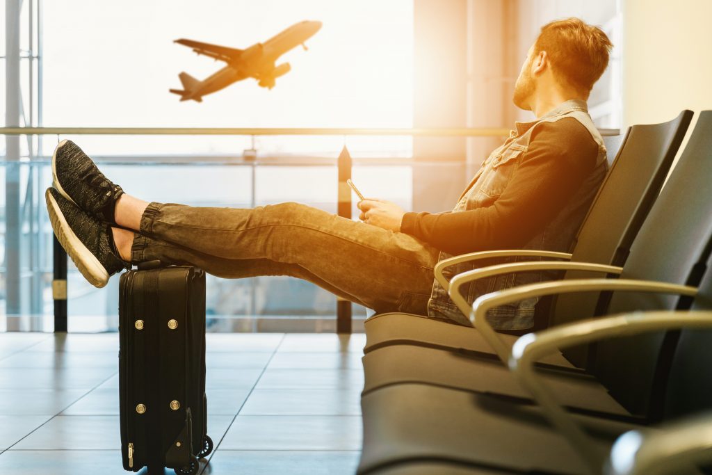 person sitting in airport with phone and suitcase